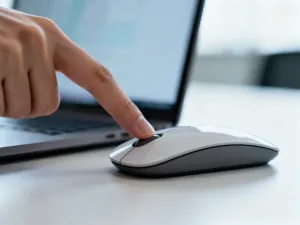 Dłoń naciskająca klawisz na nowoczesnym laptopie w jasnym, minimalistycznym biurze.